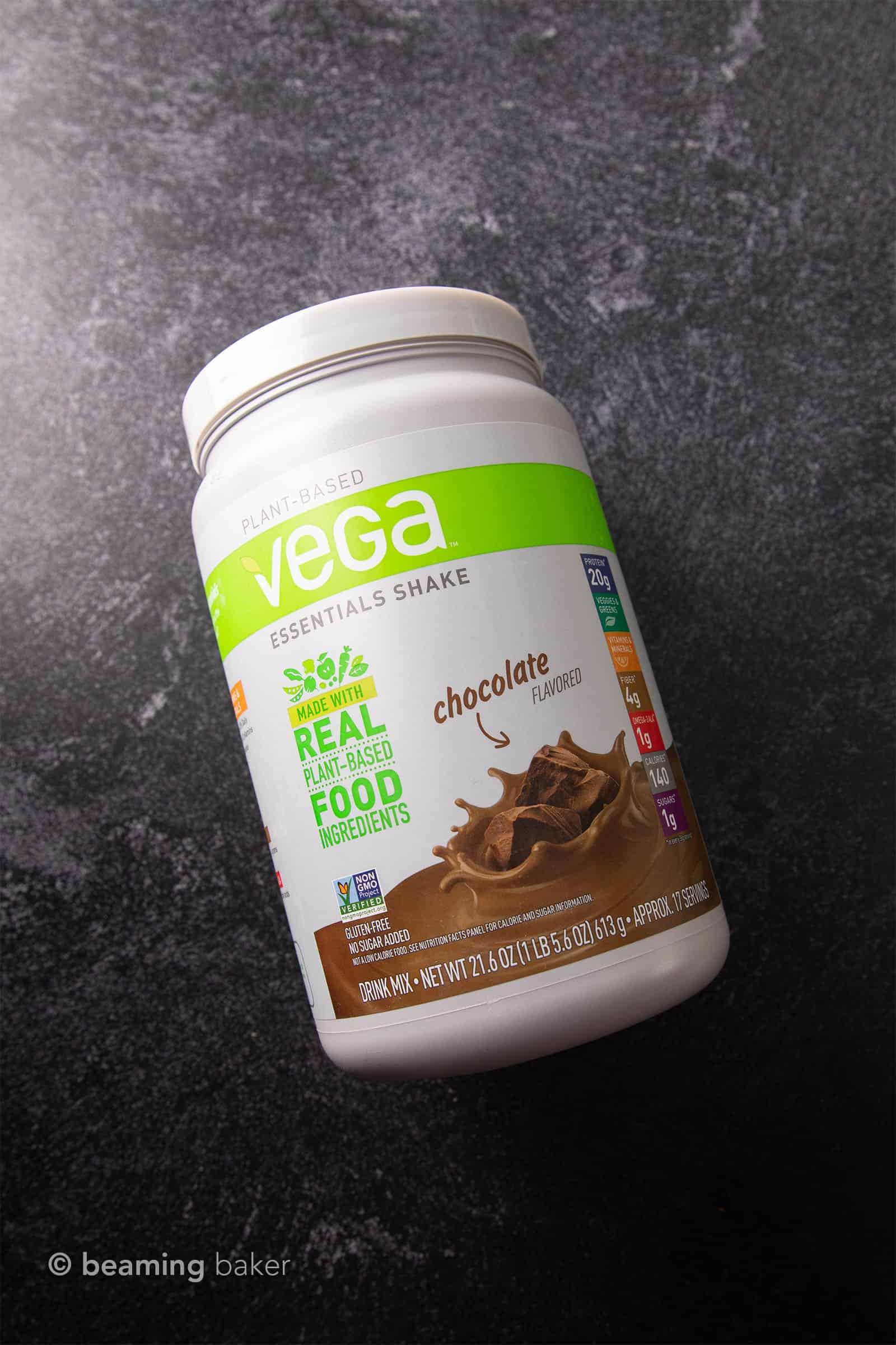 Container of Vega Essential Shake vegan chocolate protein powder on grey background