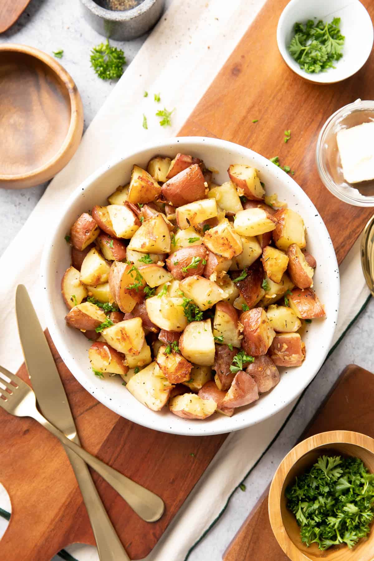 roasted potatoes with garlic on a wooden board with serving utensils