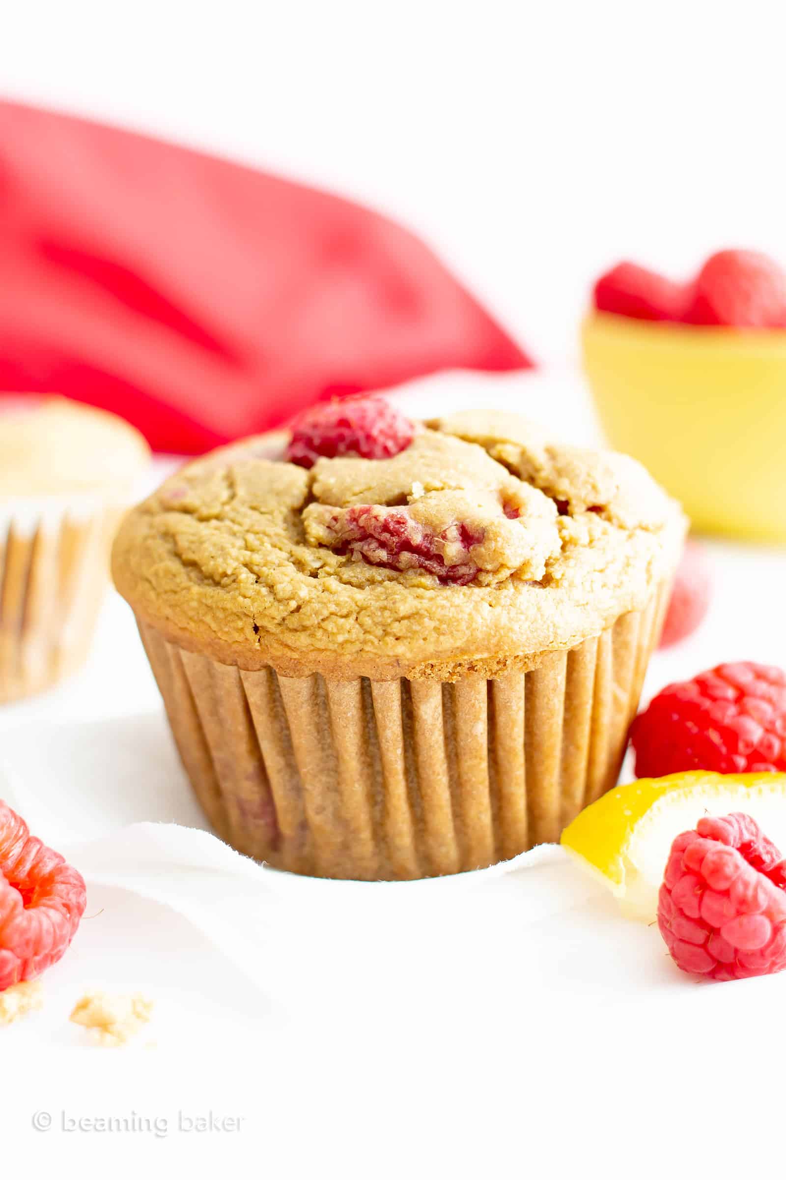 Vegan gluten free lemon raspberry muffin with raspberries on the side and yellow bowl of raspberries in the background