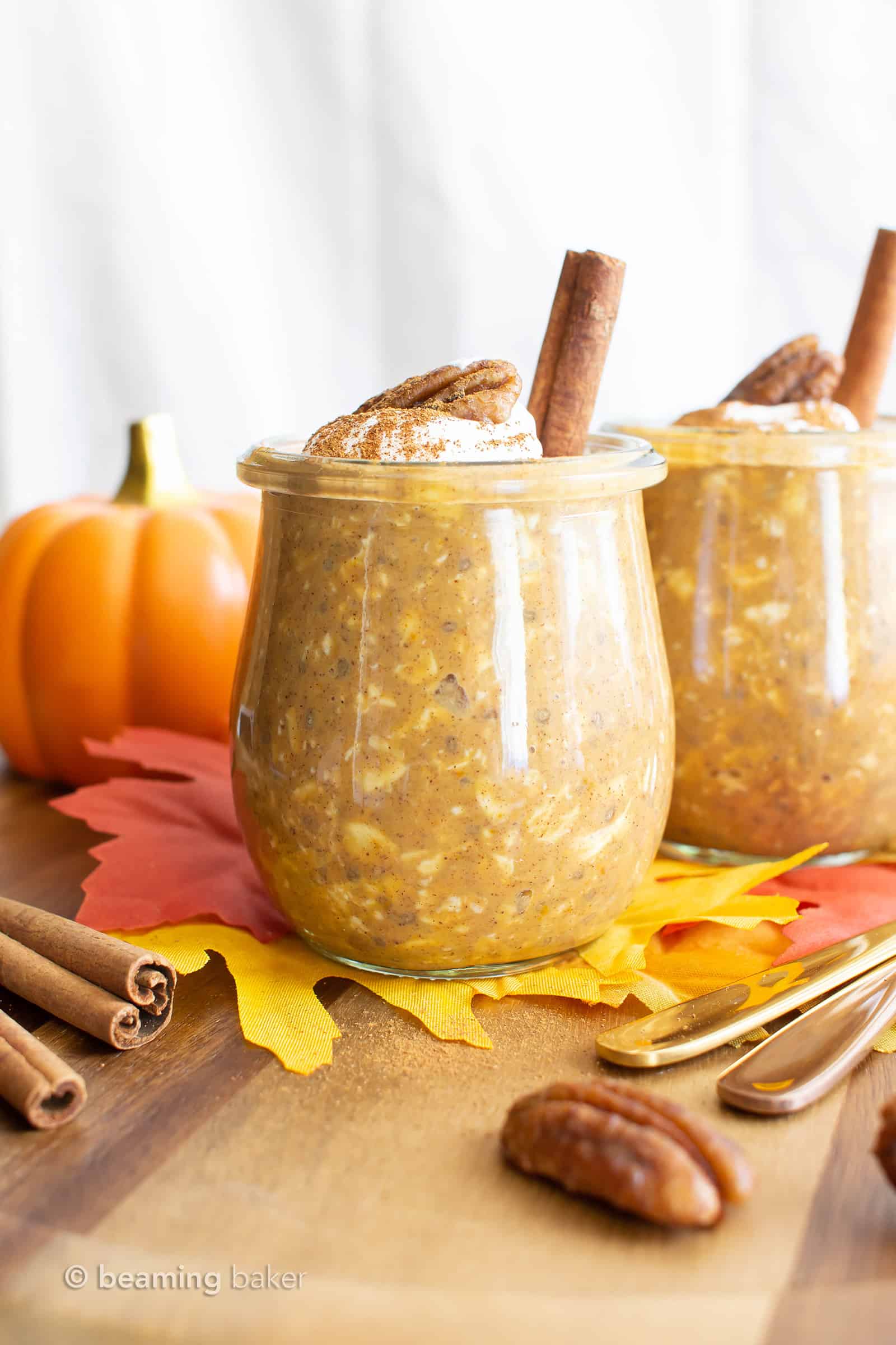 two jars filled with Pumpkin Overnight Oats, served with pecans and cinnamon sticks
