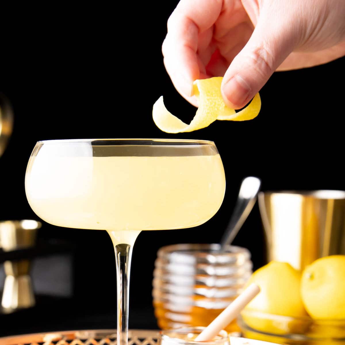 Hand adding a garnish to a Bee's Knees cocktail served in a cocktail glass