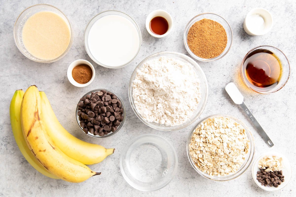 Oatmeal banana bread ingredients measured into prep bowls including bananas, flour, oats, sugar, maple syrup, and cinnamon