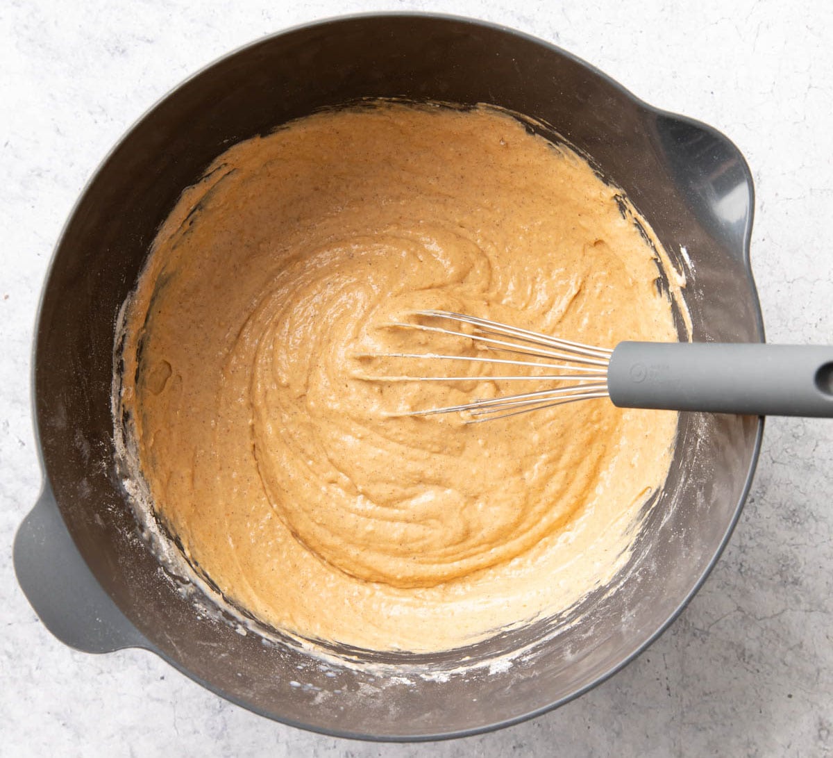 A photo showing How to Make this fall breakfast recipe – a whisk sitting in the thoroughly mixed batter