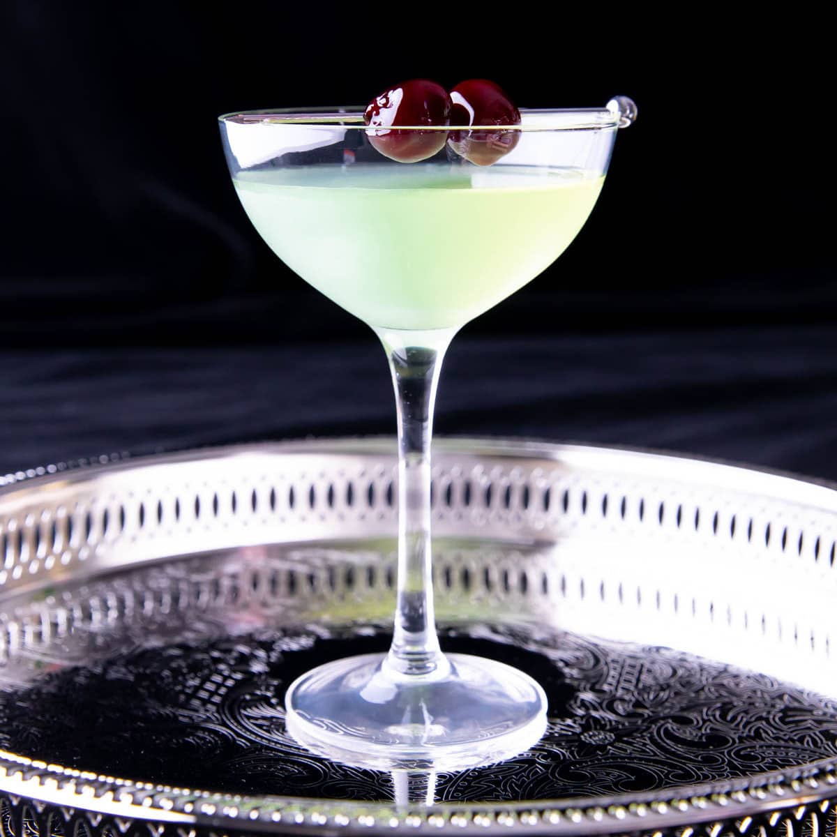 Last Word Cocktail with glowing green chartreuse and Luxardo maraschino cherry liqueur served with a brandied cherry garnish