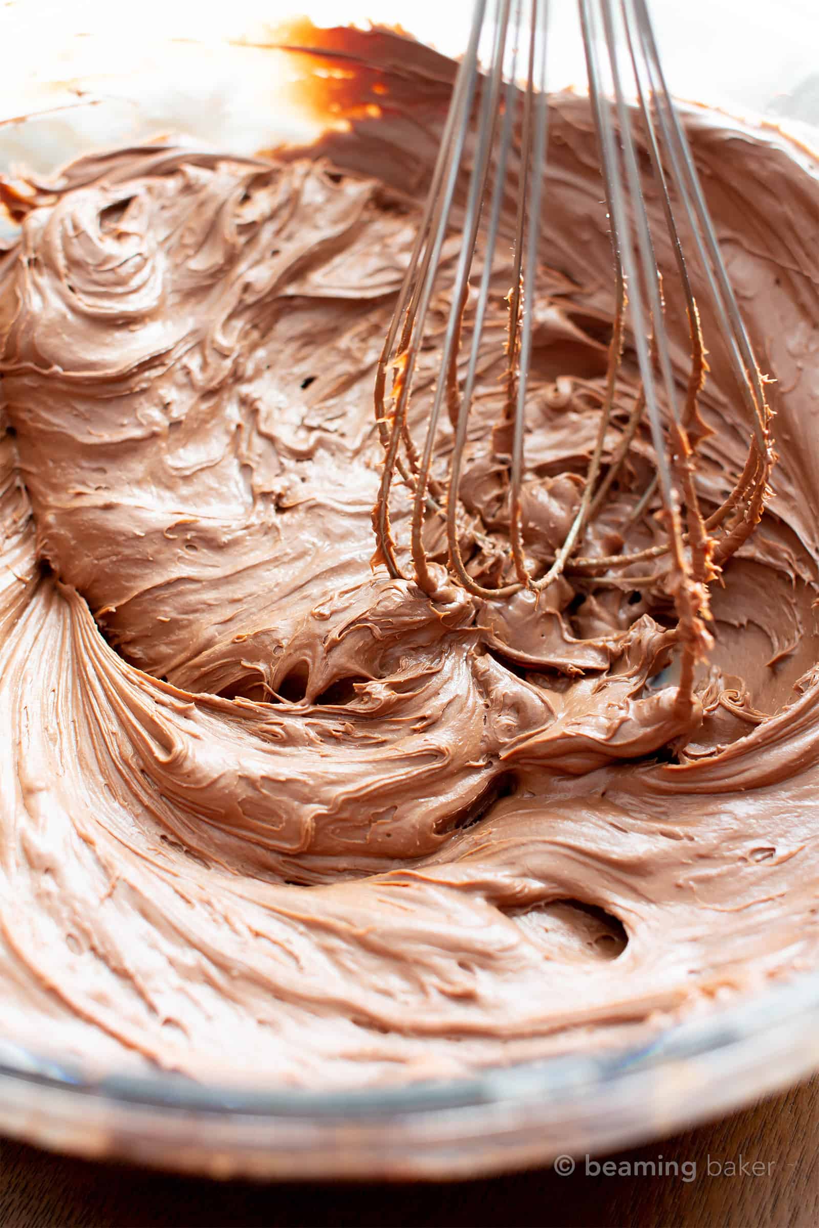 Bowl of vegan gluten free chocolate frosting with a whisk stirring the frosting